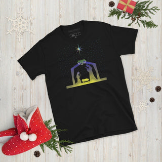 Black T-shirt with a nativity scene beneath a bright star, laid flat with Christmas decorations