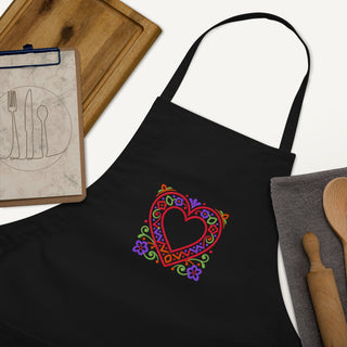 Folk Heart apron with colorful heart embroidery, black apron beside kitchen utensils.