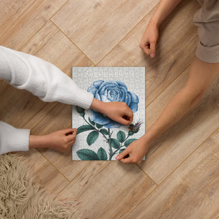 Hands assembling the Grace in Bloom blue rose jigsaw puzzle on a wooden floor.