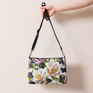 Bed of Roses crossbody bag with cream flowers, purple roses and black trim; held by its shoulder strap.