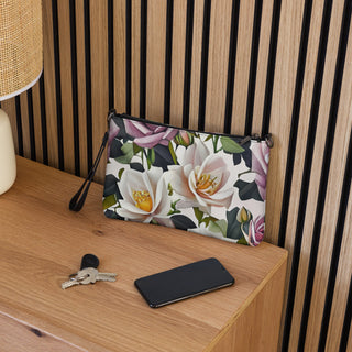 Bed of Roses crossbody bag with cream flowers, purple roses and black trim; on a shelf beside keys and a phone.