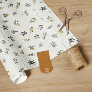 In Excelsis Deo botanical wrapping paper with greenery on a pale background, on a wrapping table with scissors and twine.