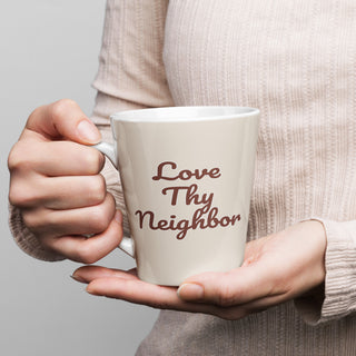 Cream-colored Love Thy Neighbor latte mug with burgundy script, held in both hands.