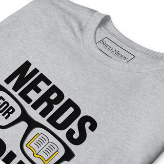 A close-up of a light heather gray t-shirt featuring a graphic print that reads 'NERDS FOR SCIENCE' with glasses and an open book illustration. The inner neck label shows the brand 'Shellmiddy'.