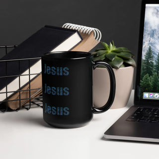Black mug on a desk with a laptop, books, and a plant.