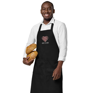 Black God Is Love apron with floral heart embroidery, worn by a model holding bread.