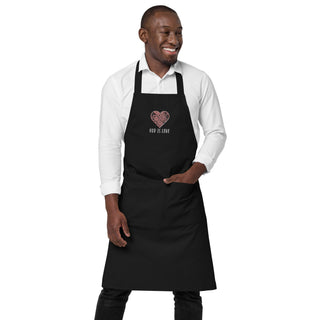 Front view of a model wearing the black God Is Love apron with one hand in its front pocket.