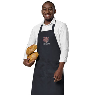Navy God Is Love apron with floral heart embroidery, worn by a model holding bread.