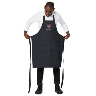 Model holding out the navy God Is Love apron to show its full shape, divided pocket and long ties.