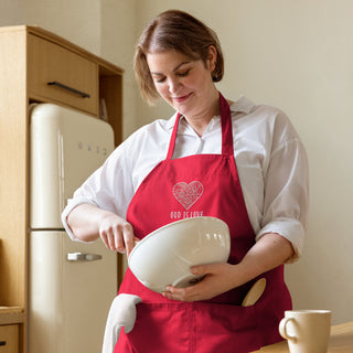 Red God Is Love organic cotton apron worn while stirring a mixing bowl in a kitchen.