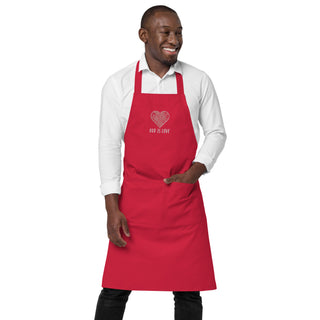 Front view of a model wearing the red God Is Love apron with one hand in its front pocket.