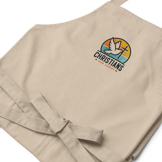 Close-up of the folded beige apron showing dove-and-cross embroidery, Christians For Christ lettering, and waist bow.