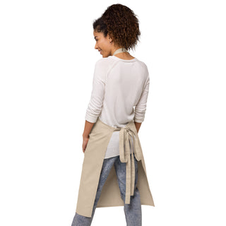 Back view of a woman wearing the beige apron, showing its neck strap and tied waist straps.