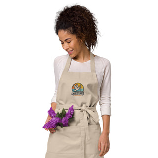 Woman wearing the beige Christians For Christ apron with purple flowers tucked into the front pocket.