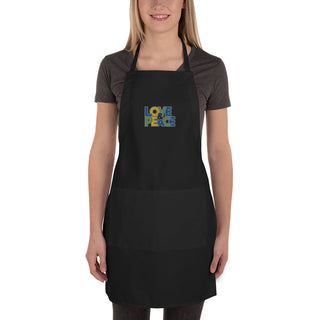 Love & Peace embroidered apron with blue, green, and yellow lettering, black apron on a model, full length.