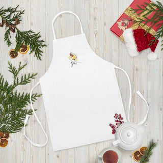 White Amazing Grace apron laid flat with Christmas greenery, gifts, and a teapot.