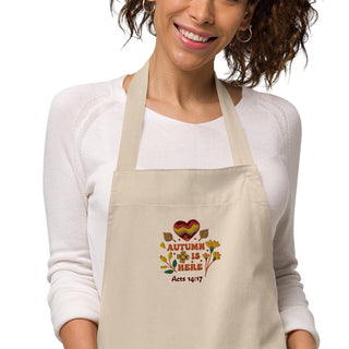 Woman wearing the natural Autumn Is Here apron with floral embroidery and an Acts 14:17 reference.