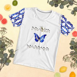 White T-shirt with Prayer Warrior lettering and blue butterflies, front laid flat among fruit and leaves